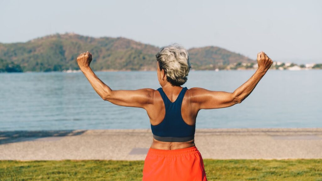 Senior gray-haired woman doing exercises in public park, sunny summer morning.