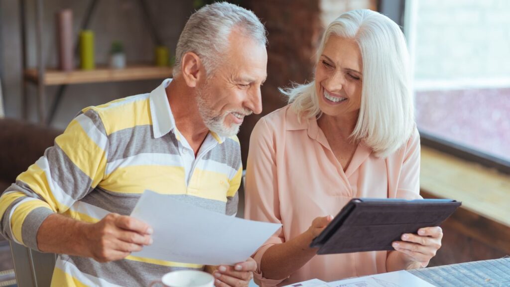 Cheerful loving aged couple involved in paperwork at home