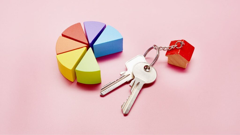 High angle view of pie chart made of colorful building blocks and keys with a small house on pink background